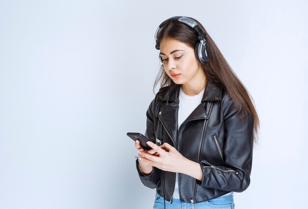 Frau mit Kopfhörern, die ihr Smartphone zum Einstellen der Wiedergabeliste verwendet.