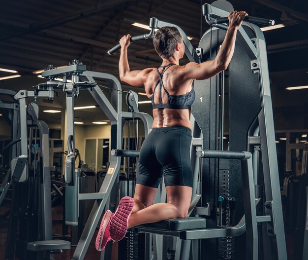 Frau mit kurzen Haaren, die Klimmzüge in einem Fitnessstudio macht.