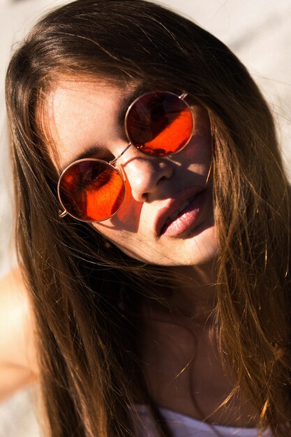 Frau mit langen Haaren in roten Sonnenbrillen sitzt auf weißem Sand