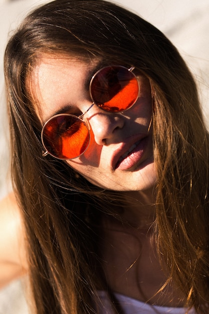 Frau mit langen Haaren in roten Sonnenbrillen sitzt auf weißem Sand