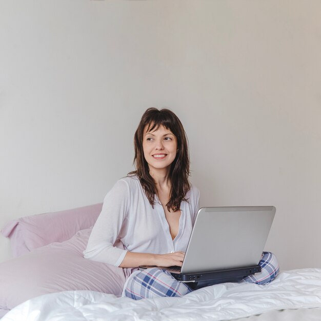 Frau mit Laptop auf dem Bett während des Morgens