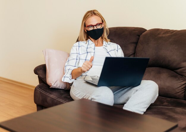 Frau mit Laptop und Baumwollmaske, die zu Hause während der Quarantäne arbeiten