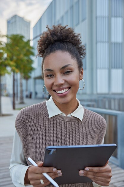 Frau mit lockigem Haar hält elektronischen Stift und Tablet erstellt Webinhalte über eine Medienanwendung auf dem Touchpad durchsucht die Website nach Online-Chats