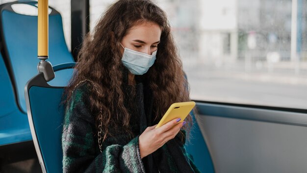 Frau mit lockigem Haar unter Verwendung ihres Handys im Bus