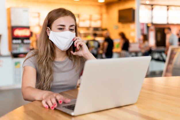 Frau mit Maske, die am Laptop an der Terrasse arbeitet