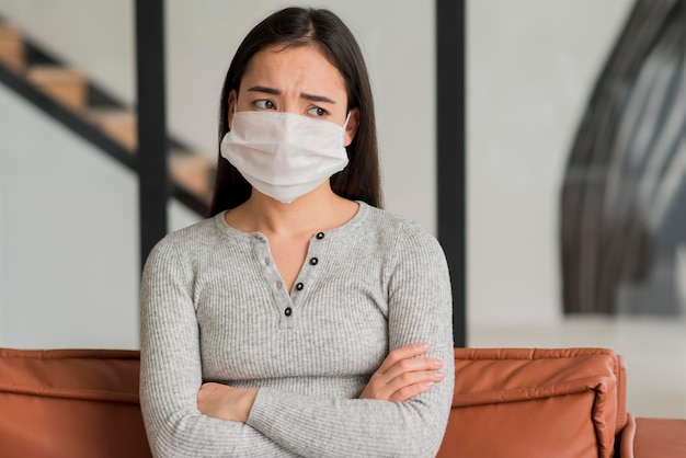 Frau mit Maske, die auf Couch sitzt