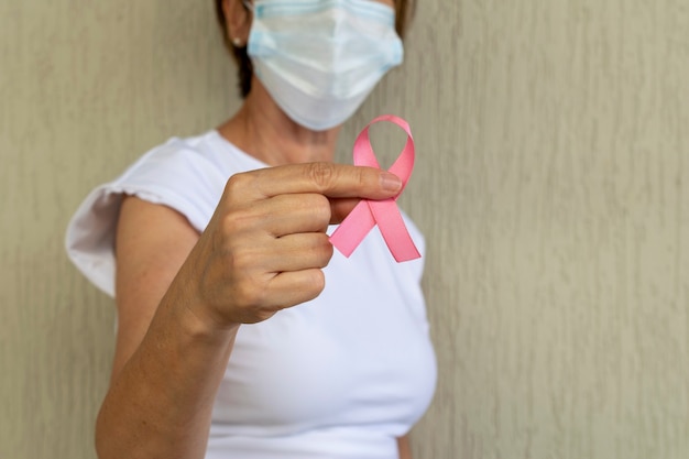 Frau mit maske hält rosa schleife in der hand brustkrebs-präventionskampagne rosa oktober