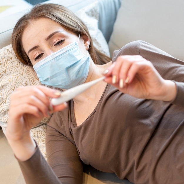 Frau mit Maske unter Verwendung eines Thermometers