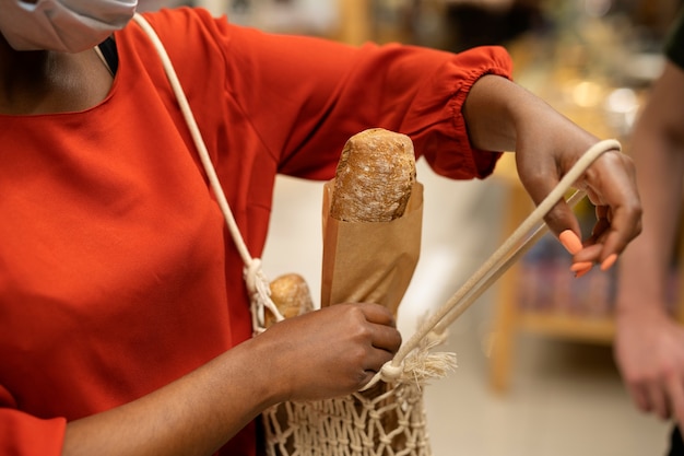 Frau mit medizinischer Maske, die Brot im Supermarkt bekommt