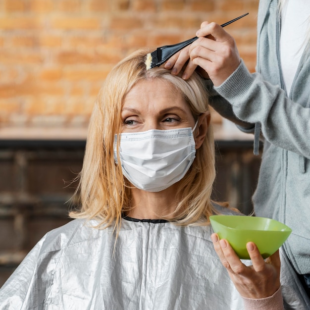 Frau mit medizinischer Maske, die ihr Haar vom Friseur zu Hause färben lässt