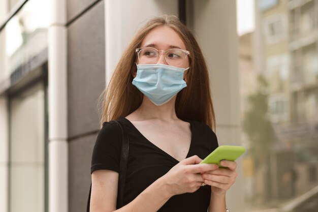 Frau mit medizinischer Maske, die ihr Telefon überprüft