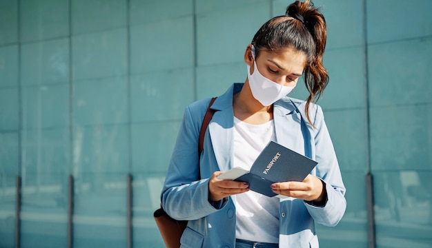 Frau mit medizinischer Maske, die ihren Pass am Flughafen während der Pandemie überprüft