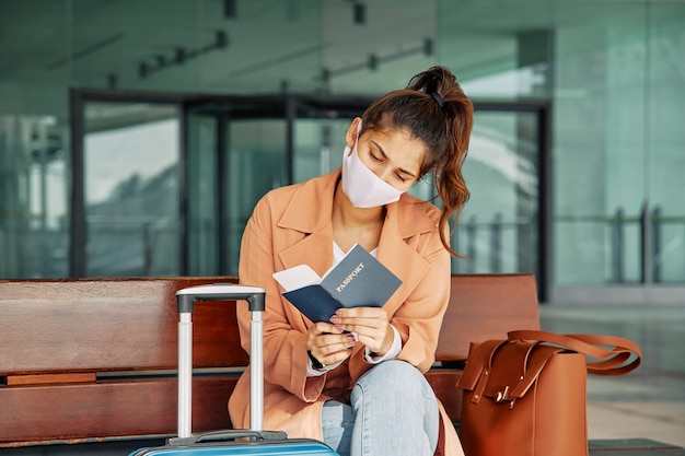 Frau mit medizinischer Maske, die ihren Pass am Flughafen während der Pandemie überprüft