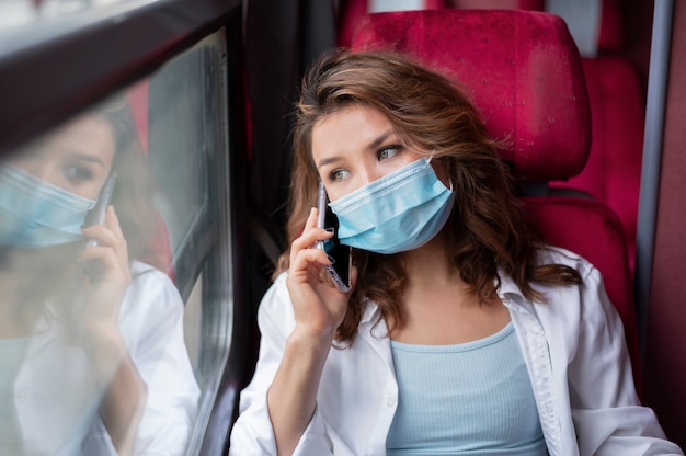 Kostenloses Foto frau mit medizinischer maske, die mit dem öffentlichen zug reist und smartphone verwendet