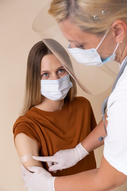 Frau mit medizinischer Maske, die nach einer Impfung einen Aufkleber am Arm bekommt