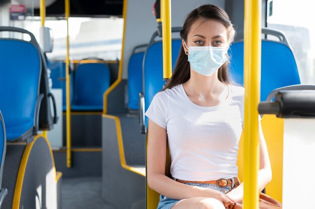 Frau mit medizinischer Maske, die öffentlichen Bus für den Transport nutzt
