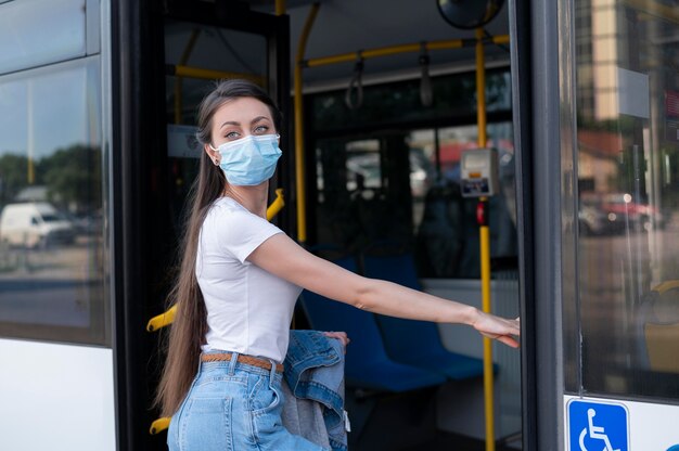 Frau mit medizinischer Maske, die öffentlichen Bus für den Transport nutzt