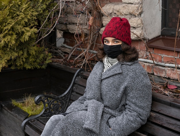 Frau mit medizinischer Maske draußen auf Bank