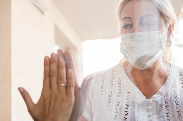 Frau mit medizinischer Maske in Quarantäne hinter Fenster