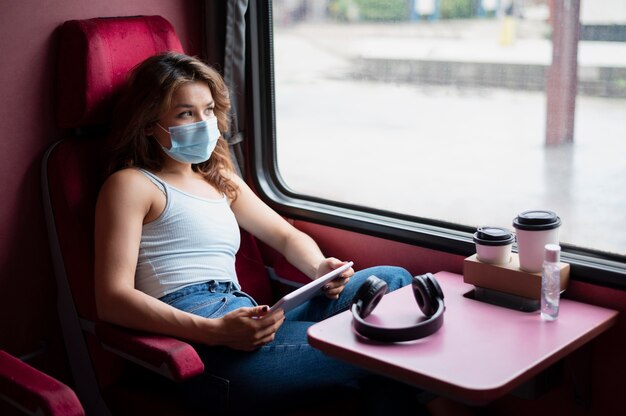 Frau mit medizinischer Maske mit Tablet während der Fahrt mit dem öffentlichen Zug