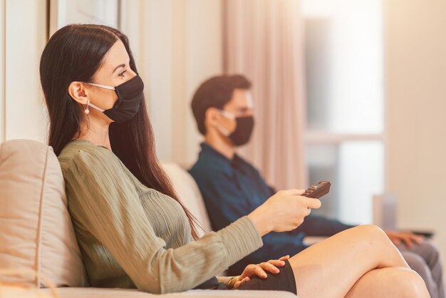 Frau mit medizinischer Maske und Fernbedienung, während sie zusammen mit ihrem Freund in der Hotellobby sitzt. Beziehung, Reisen, Coronavirus, Covid19-Konzept