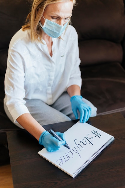 Frau mit medizinischer Maske und Handschuhen, die auf Notizbuch schreiben