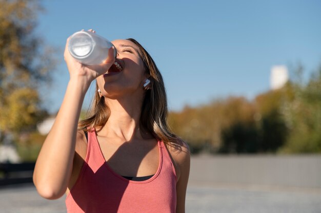 Frau mit mittlerer Schussweite, die Wasser trinkt