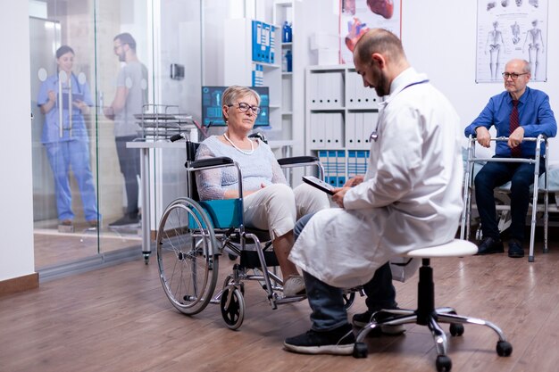 Frau mit Parkinson, die während der ärztlichen Untersuchung im Rollstuhl im Krankenzimmer sitzt