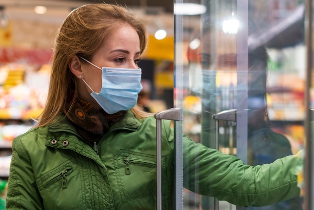 Frau mit Schutzmaske, die Produkte vom Kühlschrank nimmt