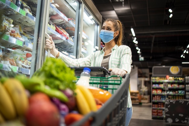 Frau mit Schutzmaske und Handschuhen, die im Supermarkt während der COVID-19-Pandemie oder des Koronavirus einkaufen