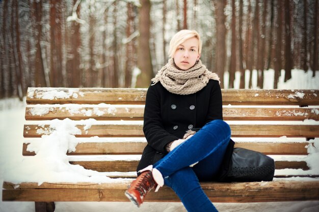 Frau mit schwarzem Mantel mit Schnee auf einer Bank sitzen