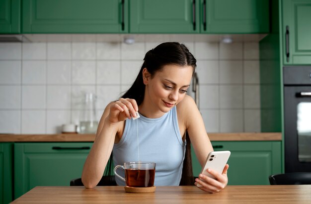 Frau mit Smartphone in einer grünen Küche