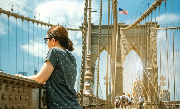 Frau mit sonnenbrille auf der suche nach stadtbild von der brooklyn bridge mit skyline von manhattan im hintergrund, in new york city