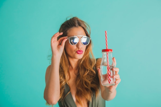 Frau mit Sonnenbrille hält Flasche mit Stroh