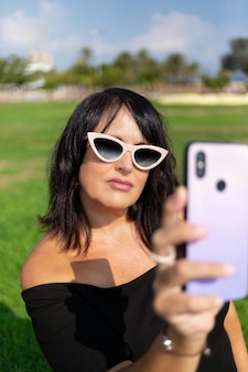 Frau mit sonnenbrille macht selfie auf dem smartphone im sonnenlicht