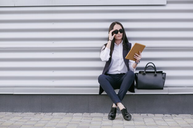 Frau mit Sonnenbrille und eine orangefarbene Tablette in der Hand