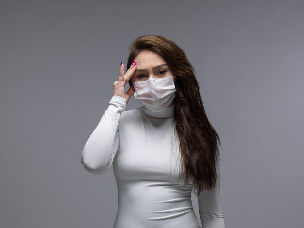 Frau mit starken Kopfschmerzen in der weißen Schutzmaske