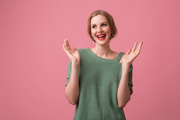 Frau mit stilvollem Make-up, roten Lippen, grünem Pullover, der auf rosa aufwirft