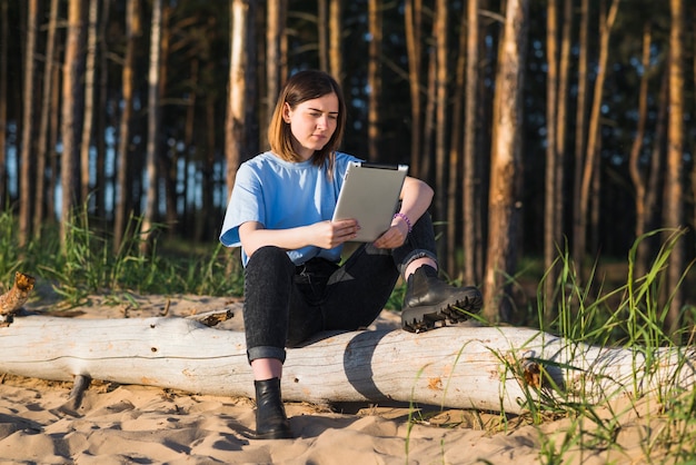 Frau mit Tablet am Baumstamm