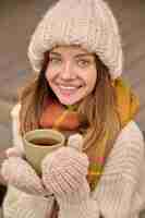 Kostenloses Foto frau mit tasse, die draußen in die kamera lächelt