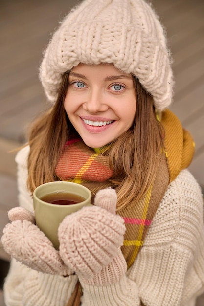 Frau mit Tasse, die draußen in die Kamera lächelt