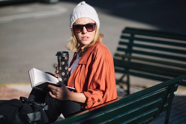 Frau mit Thermos lesen auf Bank