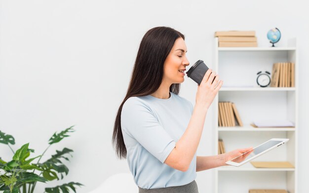 Frau mit trinkendem Kaffee der Tablette im Büro