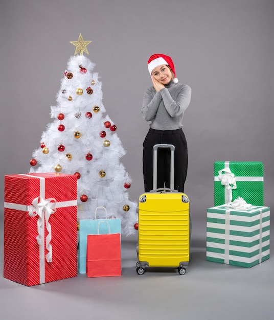 Frau mit Weihnachtsmann-Hut mit Gepäck neben Weihnachtsbaum