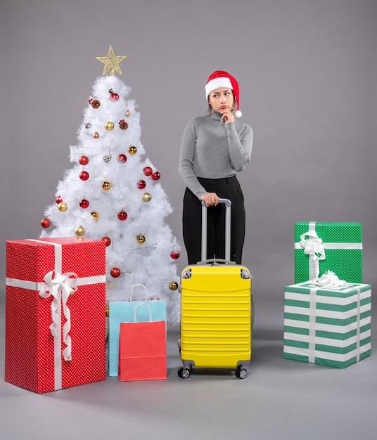 Frau mit Weihnachtsmann-Hut mit Gepäck neben Weihnachtsbaum