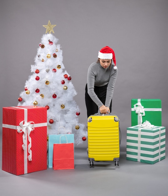 Kostenloses Foto frau mit weihnachtsmannmütze mit gepäck neben dem weihnachtsbaum