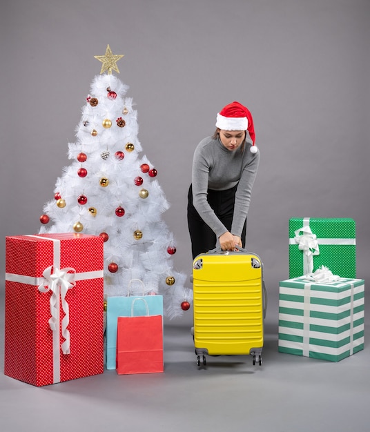 Frau mit weihnachtsmannmütze mit gepäck neben dem weihnachtsbaum