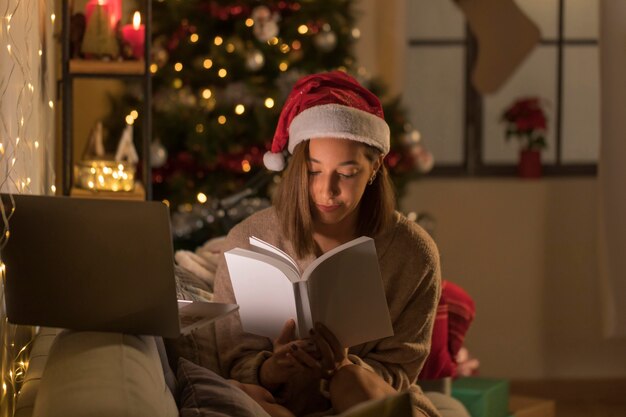 Frau mit Weihnachtsmütze, die Buch vor Laptop liest