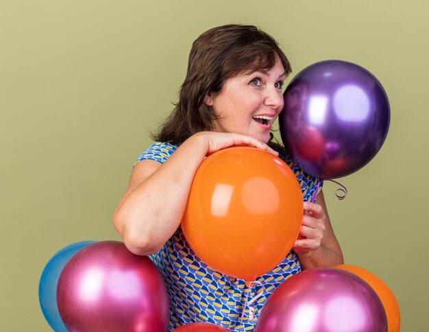 Frau mittleren Alters mit bunten Luftballons, die mit einem Lächeln auf einem glücklichen Gesicht beiseite schauen