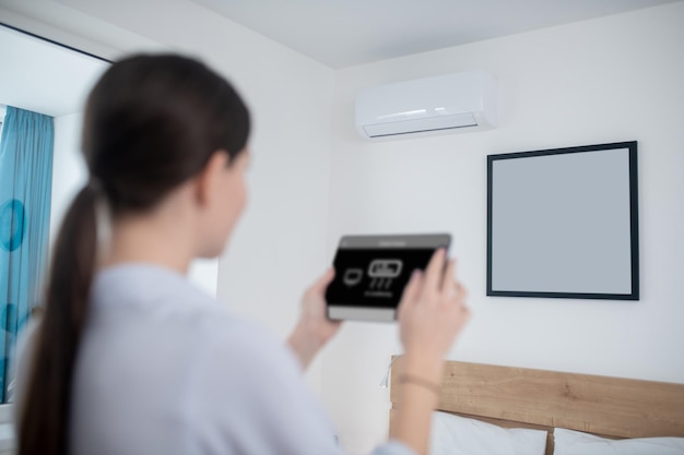 Kostenloses Foto frau schaltet eine klimaanlage mit einem tablet ein